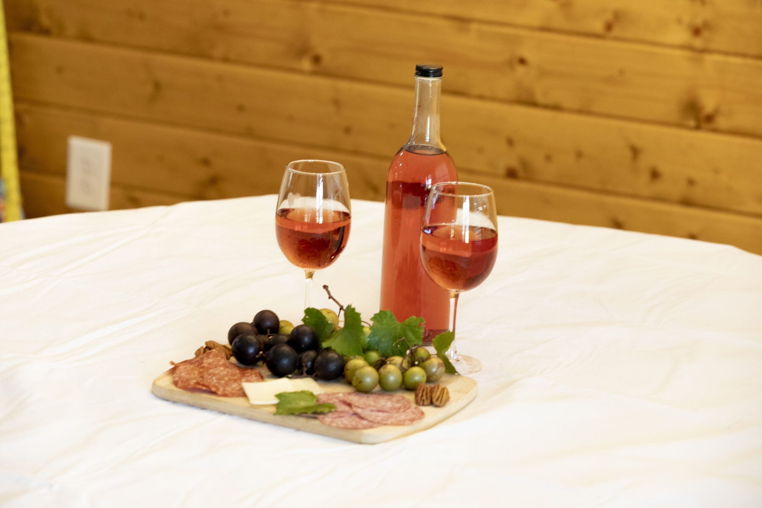 A bottle of Wandalands wine with filled glasses, cheese, and fruit on a white table