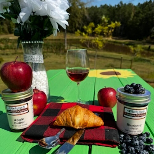 Wandalands apple butter and blueberry jelly jars on a table outdoors with fresh apples