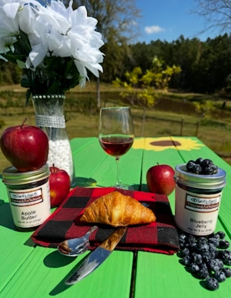 Wandalands apple butter and blueberry jelly jars on a table outdoors with fresh apples